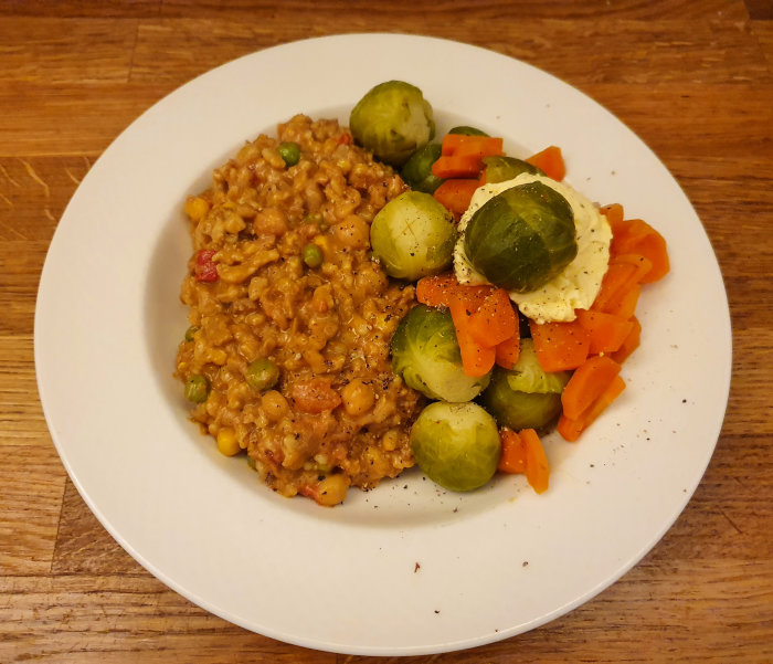 Tallrik med curry-havreris och kokta grönsaker, toppad med smör och kryddad brysselkål.