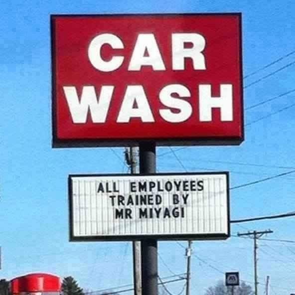 Skylt med texten "CAR WASH" överst och "ALL EMPLOYEES TRAINED BY MR MIYAGI" på informationstavlan nedanför.