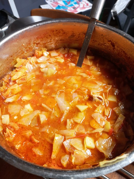 En stor gryta fylld med kålsoppa, hackad kål och potatis synlig, matlagningsyta i bakgrunden.