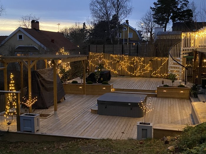 Träaltan utomhus dekorerad med ljusslingor, möbler och växter under kvällstid i vintermiljö.
