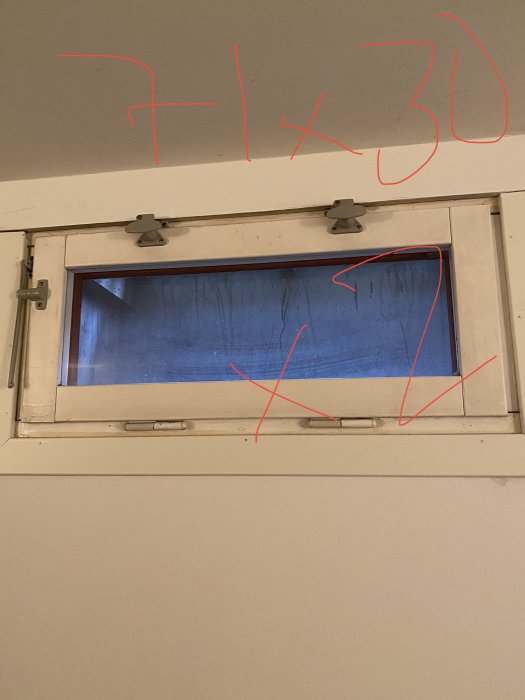 Källarfönster under marknivå med röda märkningar på mått för ventilation.