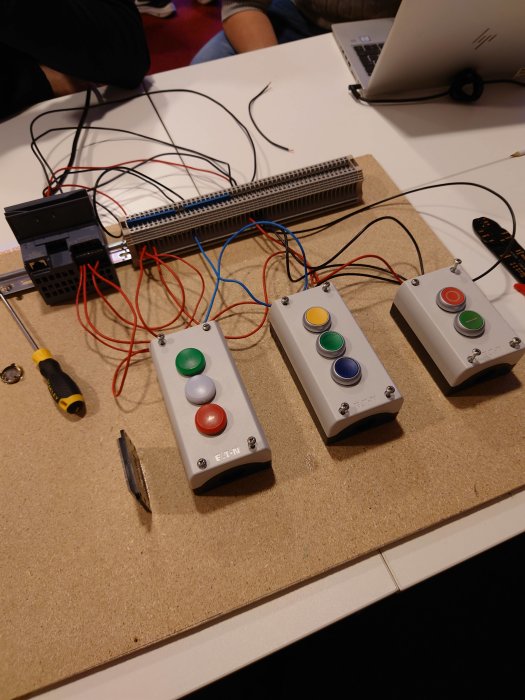 Elektronikprojekt med kopplingsbräda, kablar och tre stycken knappmoduler med färgade knappar på ett bord.