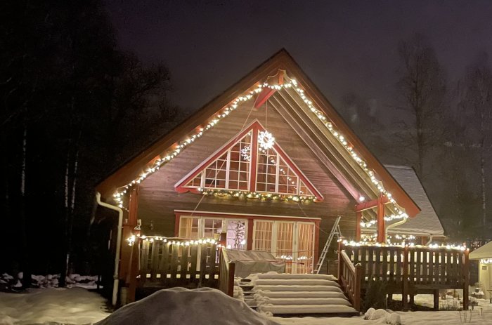 Trähus med julbelysning och en stjärnformad lampa monterade på dess gavel och räcken under kvällen.