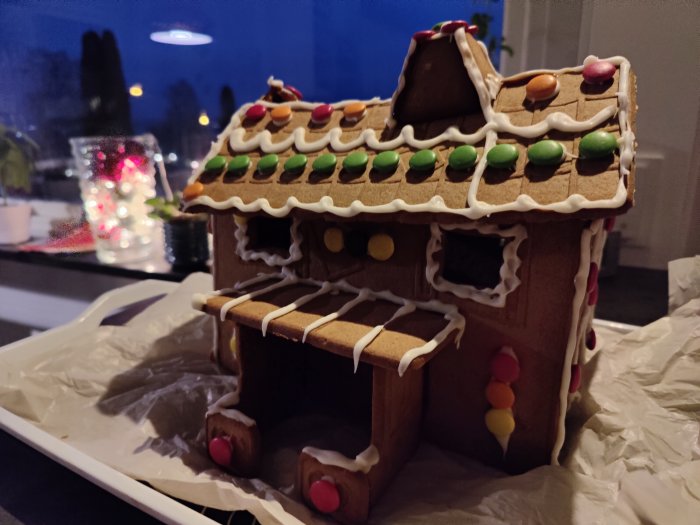 Hemgjord pepparkakshus med säckande tak och godisdekorationer på ett köksbord.