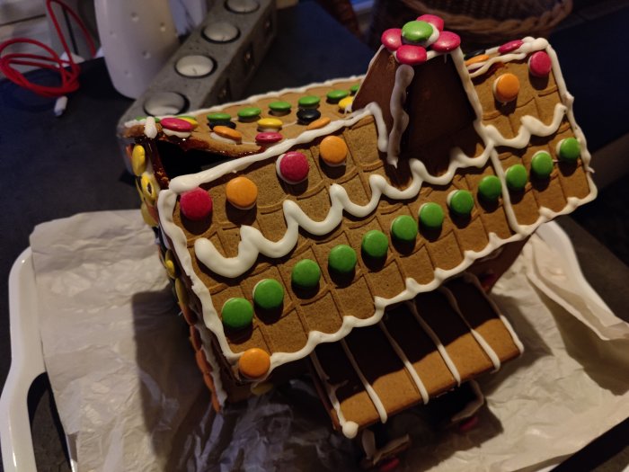 Pepparkakshus med sjunkande tak dekorerat med godis och glasyr på en vit bricka.