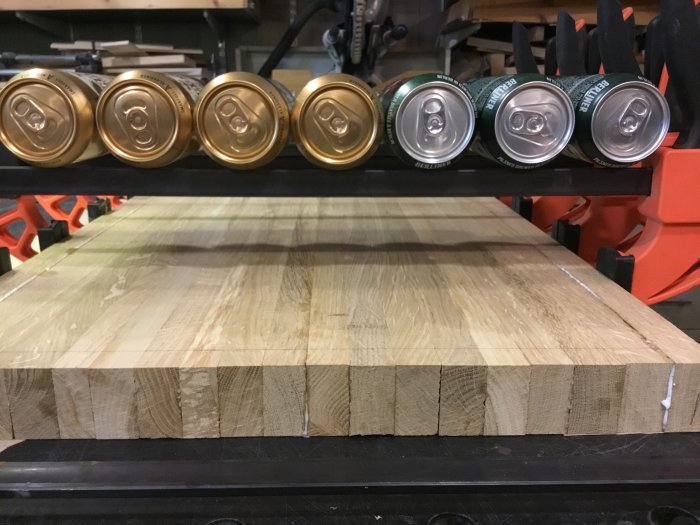 Åtta ölburkar uppradade på en träplanka i ett verkstadsrum, fyra guldiga och fyra gröna.