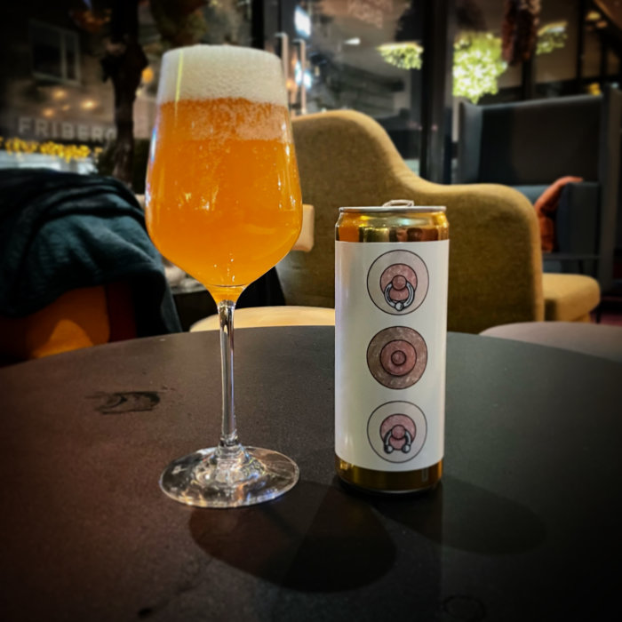 Ett glas öl och en ölburk på ett bord med en suddig inomhusmiljö i bakgrunden.