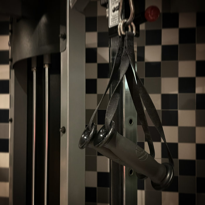 Gymutrustning med handtag och vajrar mot svartvit rutig bakgrund.