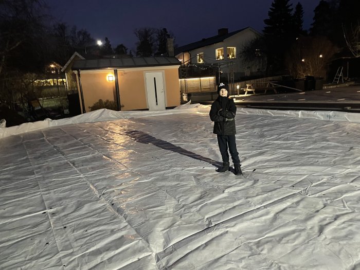 Person på en hemmagjord isbana i trädgården under kvällsbelysning.