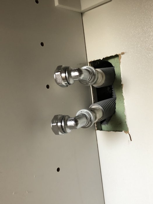 Vattenrör sticker ut från ett hål i väggen, täckt med temporära pluggar, redo för ny blandarinstallation.