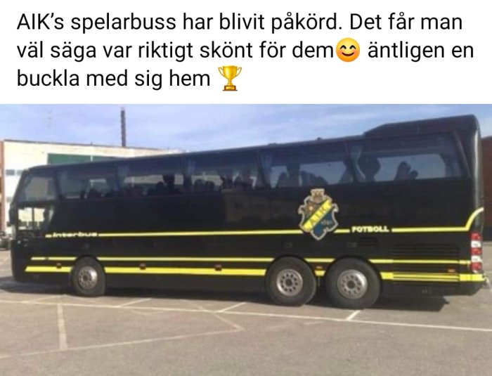 Svart och gul spelarbuss med lagets emblem, parkerad med synlig skada på bakänden.