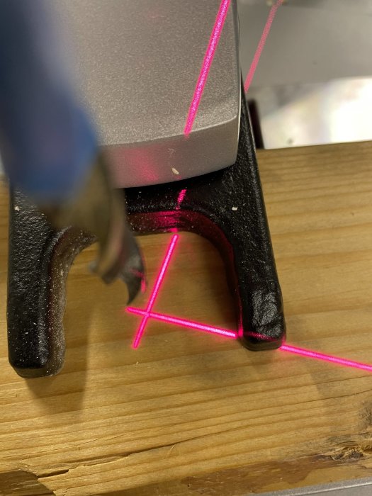 Laserverktyg som projicerar en röd korslaserlinje på ett trägolv.