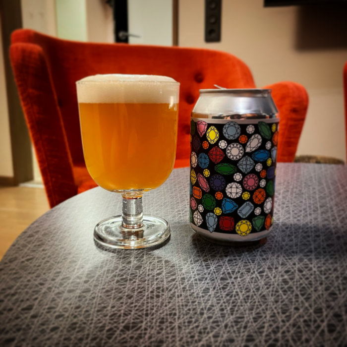 Ett glas med ljus öl och en färgglad burk på bord framför en orange stol.