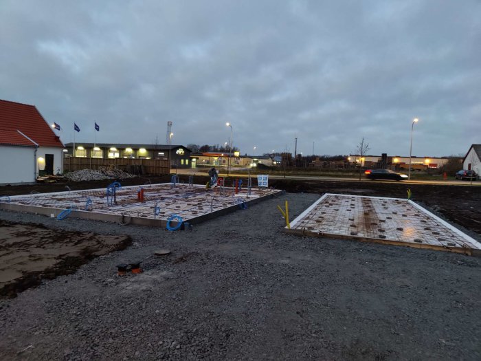 Förberedd hus- och garagegrund med armering och rörledningar, i en öppen byggplats.