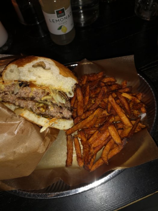 Halväten hamburgare på tallrik med söt-potatis pommes och flaska lemonad i bakgrunden.