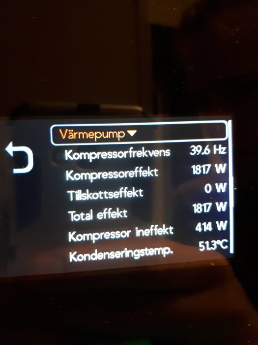 Display på värmepump som visar kompressorfrekvens och olika effektnivåer i mörkt rum.