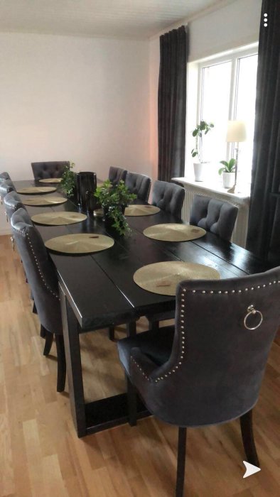 Ett långt svart matbord med stolar och dekorationer i ett ljust rum.
