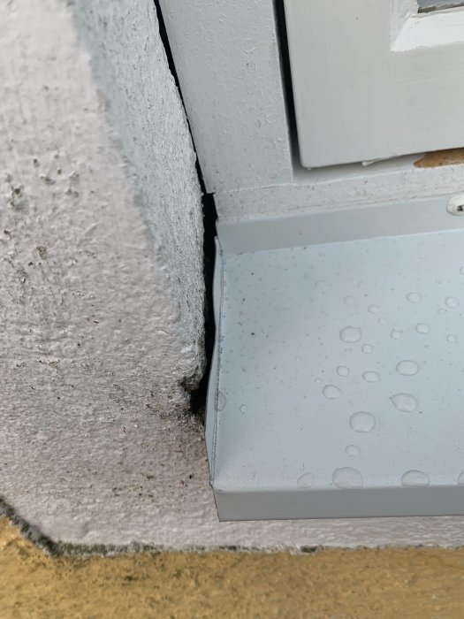 Närbild på ett renoverat fönster med synligt gap mellan plåtkanten och putsad vägg, samt ojämn fogning.