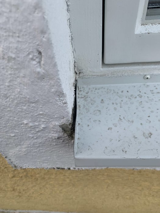 Närbesiktning av ett renoverat fönsters kant med särskilt fokus på gapet mellan plåtblecket och putsen samt på det ojämna vecket.