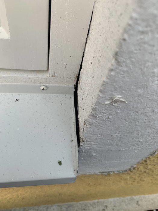 Närbelägen vy av en ojämn kant där fönsterbleck och putsad fasad möts, med varierande gap och synligt veck på plåten.