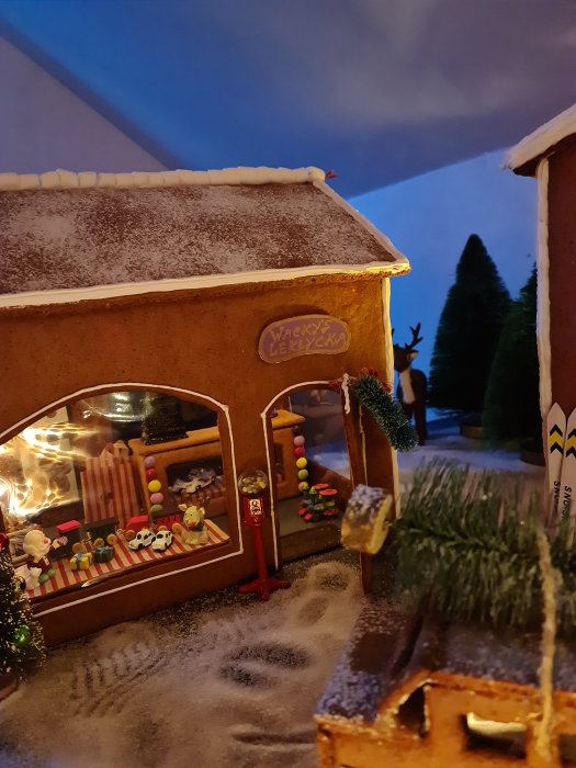 Handgjord pepparkaksby med snötäckt tak, figurer i fönstret och en julgran.