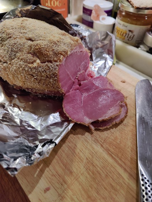 Julskinka med knaperstekt svål på skärbräda bredvid kniven, med julprodukter i bakgrunden.