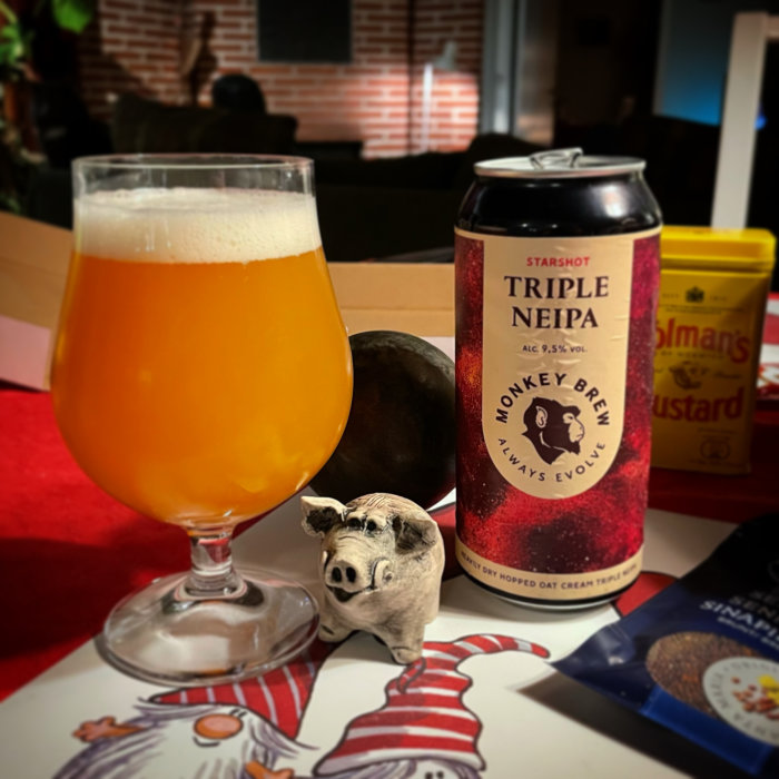 Ölglas med öl bredvid en ölburk med texten "Monkey Brew", en senapsburk och en grisknorrfigur på en kokbok.