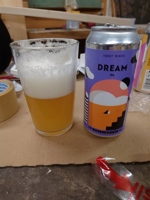 En ölglas med skum bredvid en Fuerst Wiacek Dream IPA ölburk på ett bord.