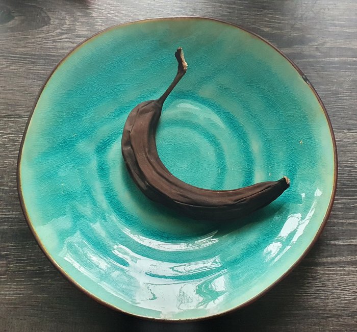 En övermogen banan på en turkos keramiktallrik mot en mörkt träliknande bakgrund.