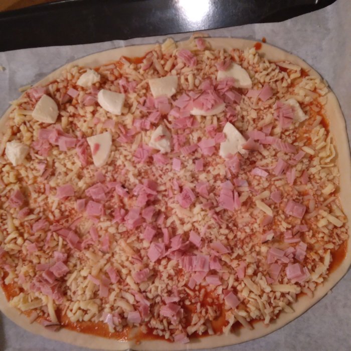 Ogräddad pizza med skinka och ost före bakning.