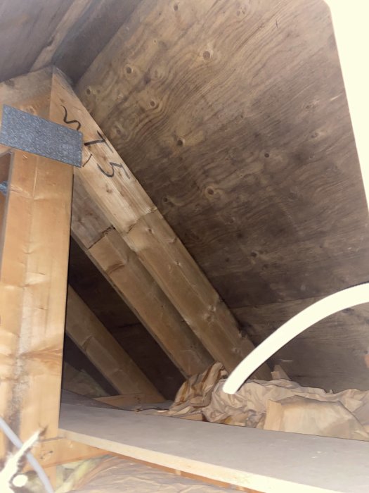 Utsikt av en vind med träbjälkar, isolering och plywood. Otillräcklig belysning och begränsad åtkomst.