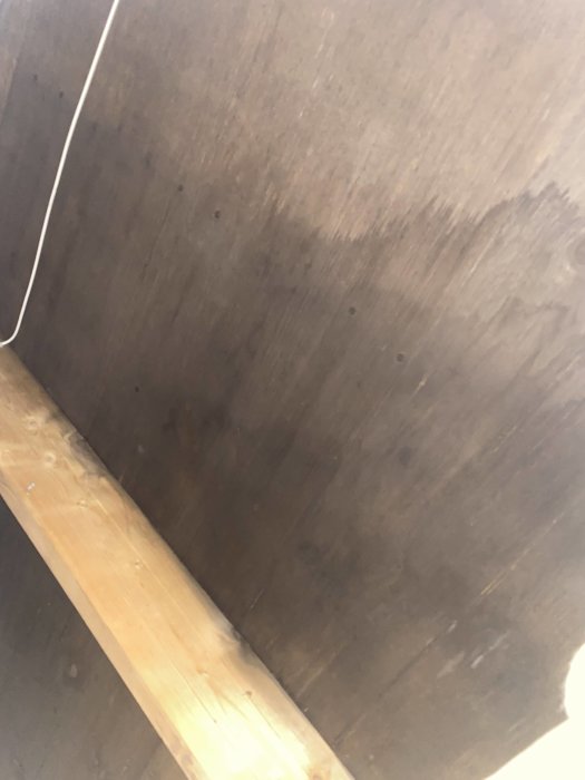 Delvis synlig träbjälke och mörkt takområde på en vind som behöver inspektion.