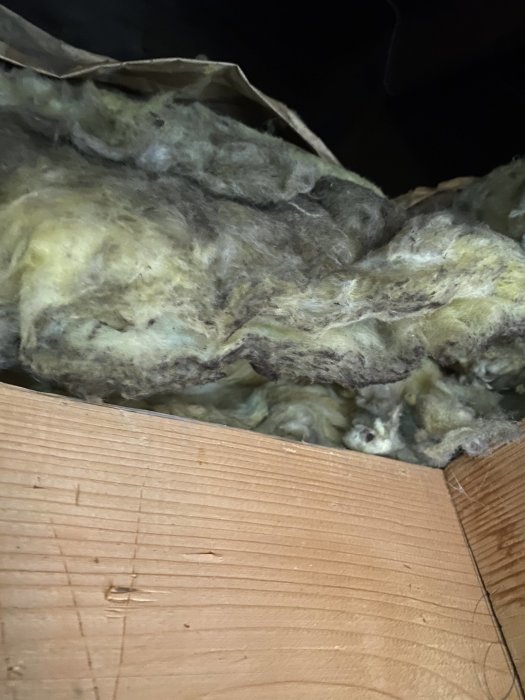 Bild av isoleringsmaterial och träbjälkar på en vind i svagt ljus.