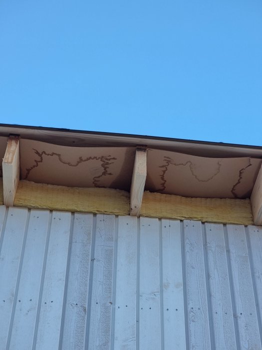 En bild av ett hus hörn som visar takkonstruktion och vattenskador på undertaket.