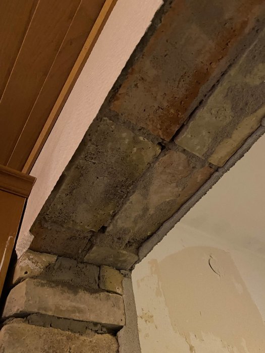 Tegelsten runt en dörröppning i ett hus, synlig efter borttagning av sidotäcklister, vilket visar en äldre konstruktionsmetod.