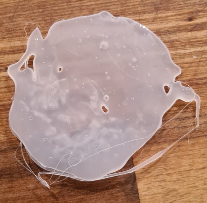Självhärdande smältlim som lossnat i form av en kaka på ett träunderlag.