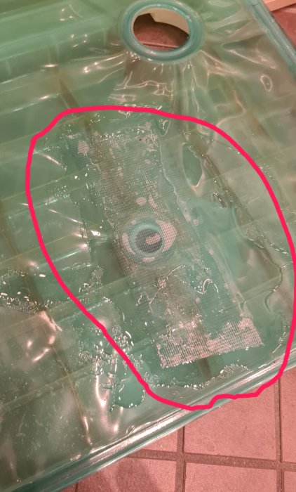 Grön plast med misslyckad smältlimsreparation markerad med röd cirkel.