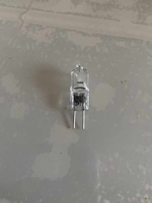 Halogenlampa med två stift på en ljus kaklad yta.