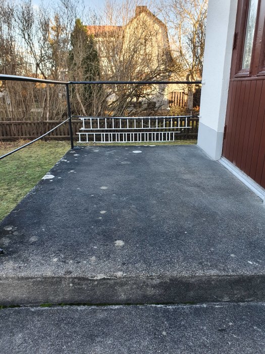 Betongtrappa med mörk, tjärliknande yta och tecken på frostsprängning, intill ett hus och en vit räcke.