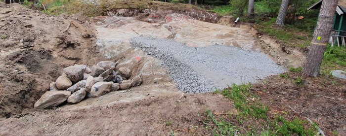 Grundarbete för hus och pool med grus och synliga berg på en tom byggplats.