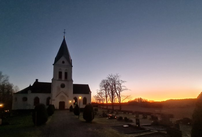 Kyrka med kyrkogård i förgrund vid solnedgång med klar himmel.