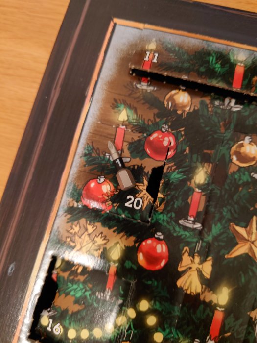 Julkalender med öppnade luckor visande gran med juldekorationer, delvis skadad.