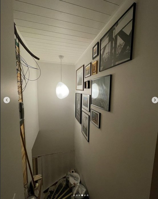 Trappa med nygrundade vita väggar och inramade bilder, vit taklampa, renoveringsmaterial på golvet.