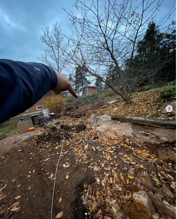 Person pekar på ett bergigt område med löv och jord där uppröjning och förberedelse för bergspräckning äger rum.