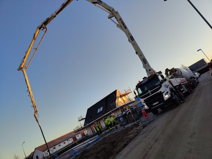 Betongbil och betongpump vid husbygge tidig morgon med arbetare som förbereder gjutning av platta.