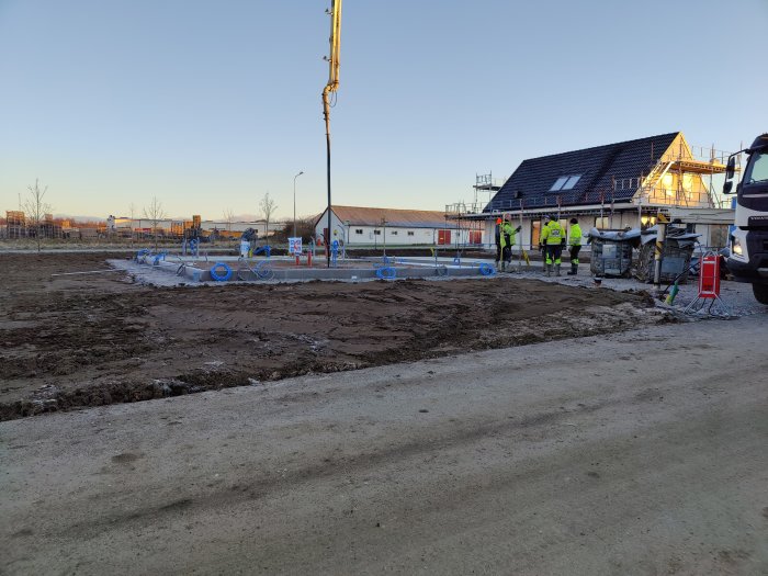 Nybetongad platta med betongbil och arbetare i arbete vid gryning.