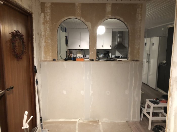 Två valvbågade öppningar i en vägg under renovering med synligt kök i bakgrunden.
