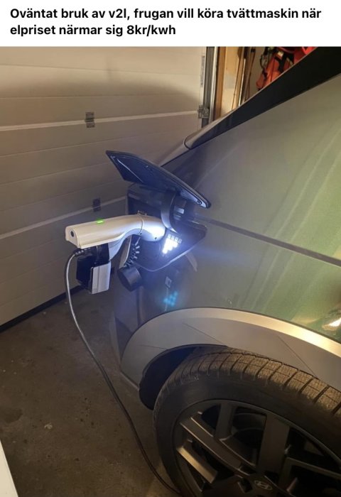 Elbil parkerad i garage med en laddkabel kopplad till en bärbar enhet som lyser upp.