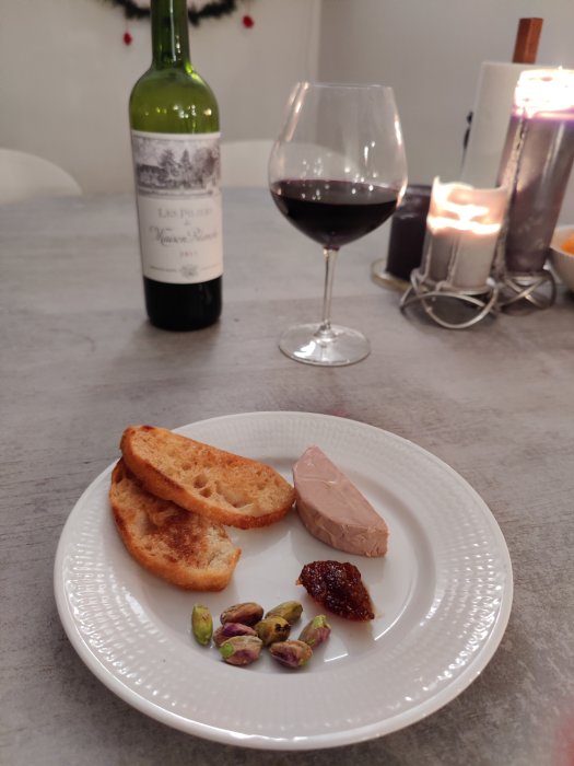 Vittallrik med gåslever, rostat bröd, fikonmarmelad, pistaschnötter och ett glas rödvin.