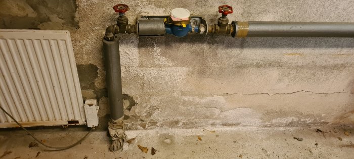 Vattenledningsrör och gammal elradiator i ett kallgarage.